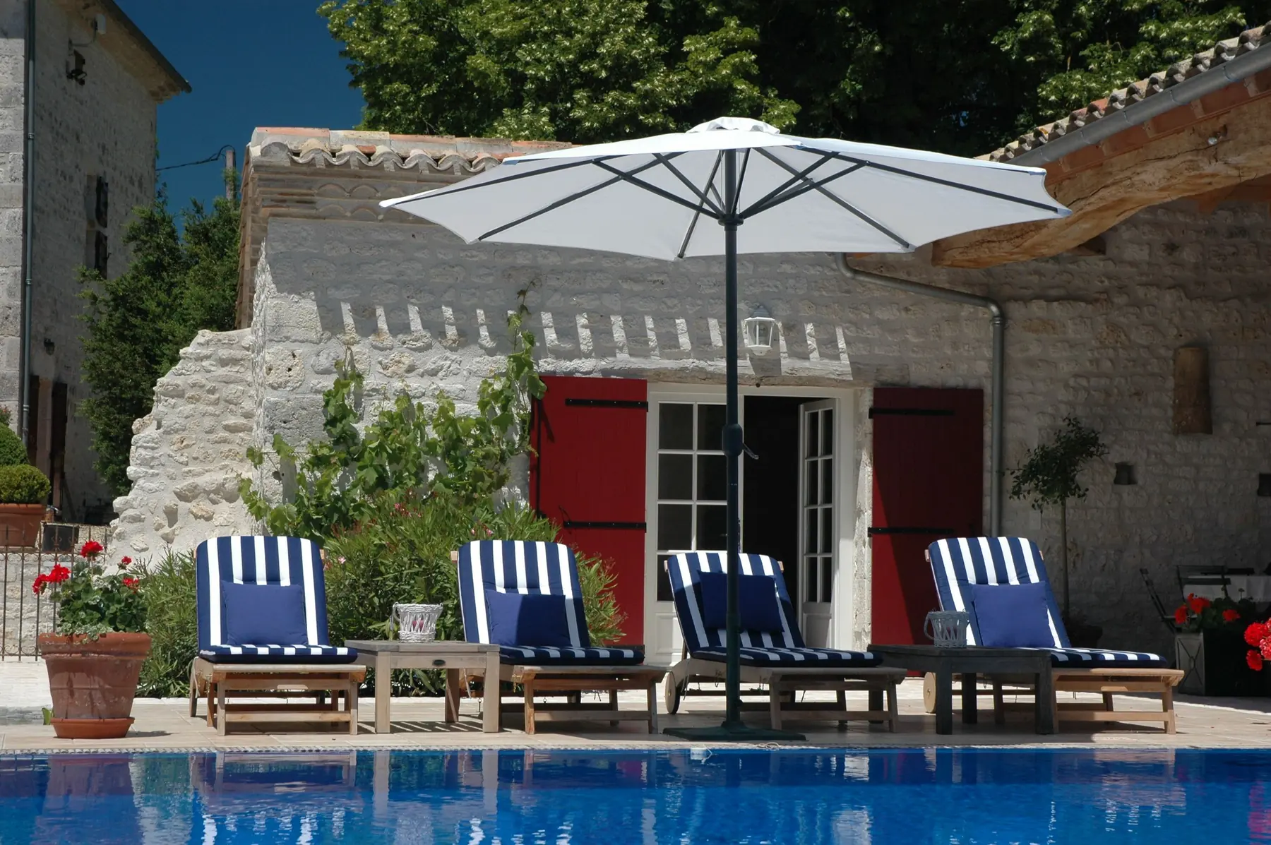 Maison blanche aux volets rouges, transats rayés au bord de la piscine
