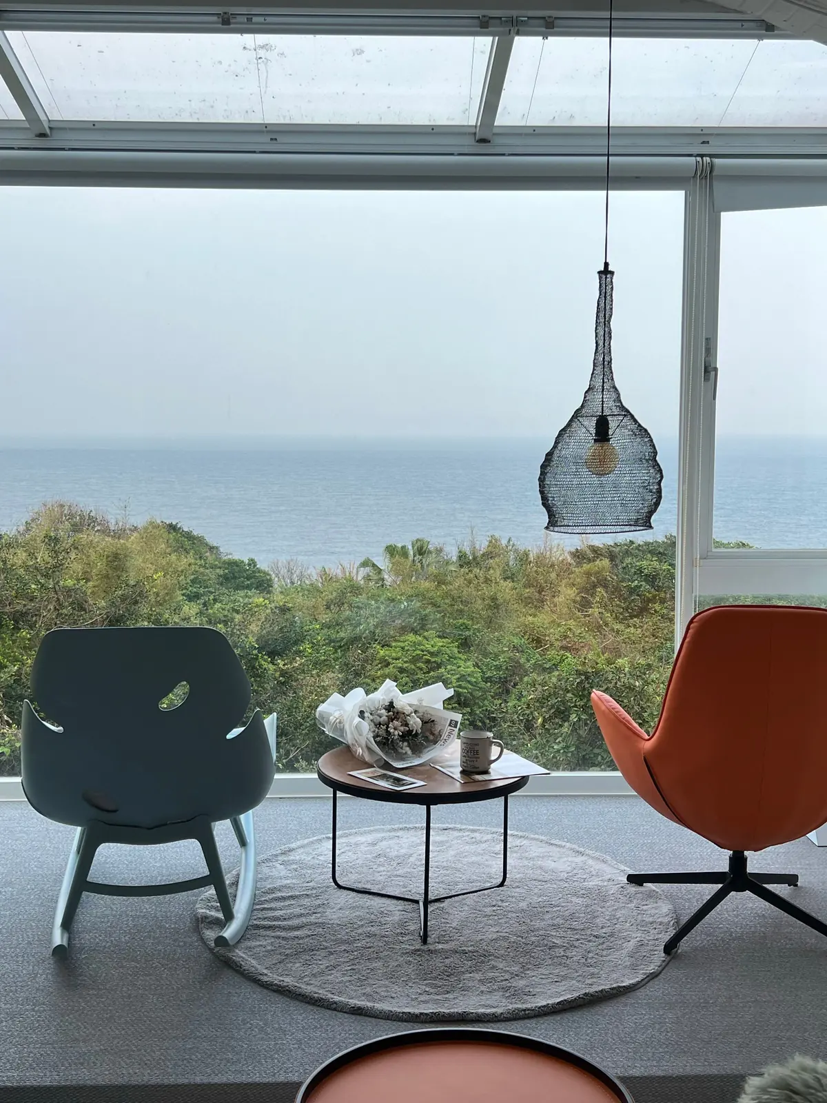 Salon vitré face à l'océan, deux fauteuils orange et une table basse