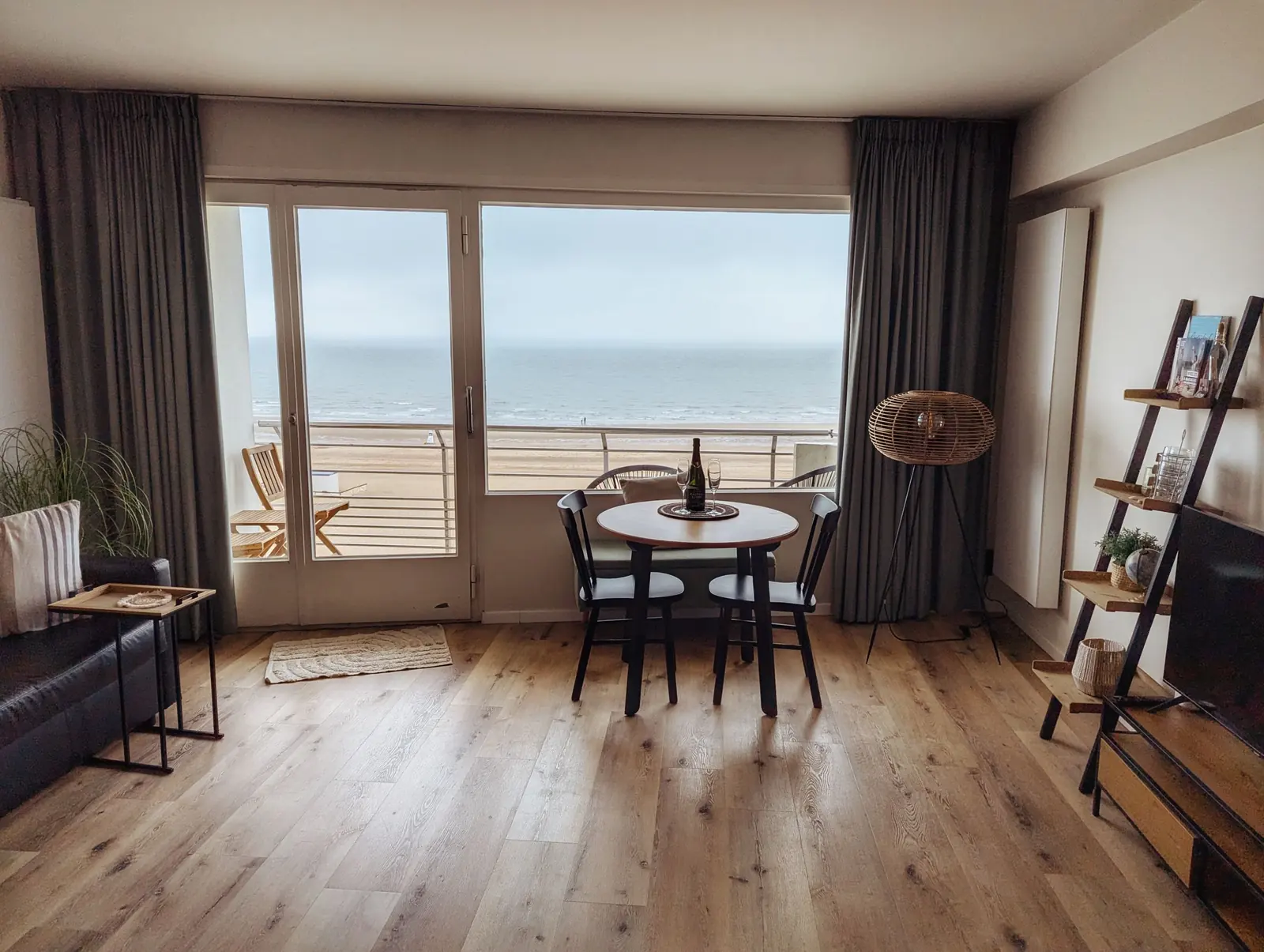 Séjour au parquet clair, table ronde devant une baie vitrée sur la mer