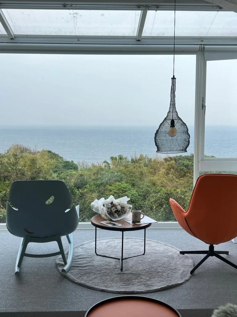 Salon vitré face à l'océan, deux fauteuils orange et une table basse