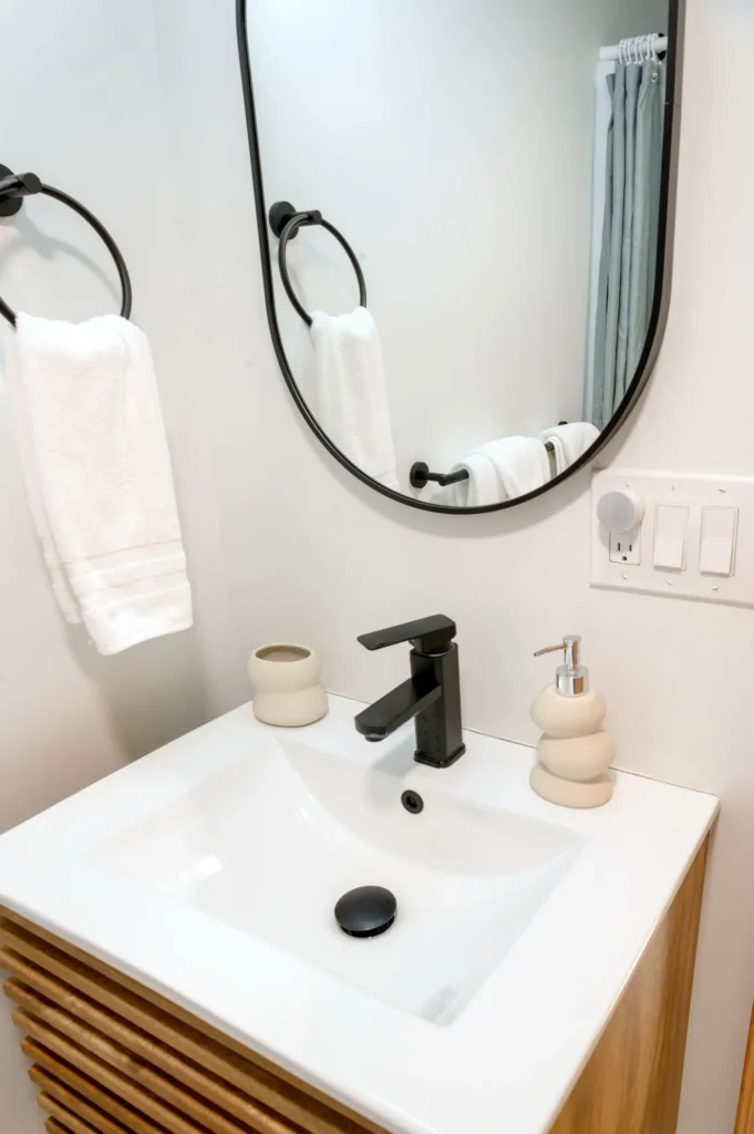 Salle de bain : vasque blanche sur meuble en bois, miroir rond